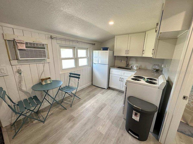 kitchen featuring white fridge, light hardwood / wood-style floors, sink, wooden walls, and white cabinets