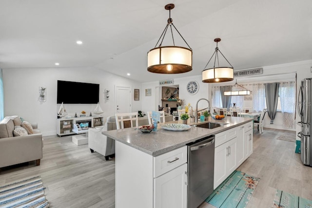 kitchen featuring decorative light fixtures, appliances with stainless steel finishes, a kitchen island with sink, sink, and white cabinets