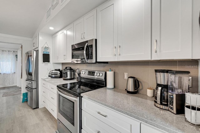 kitchen with white cabinets, tasteful backsplash, appliances with stainless steel finishes, light wood-style floors, and light stone counters