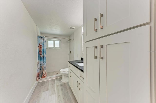 bathroom featuring curtained shower, hardwood / wood-style floors, toilet, vanity, and a textured ceiling