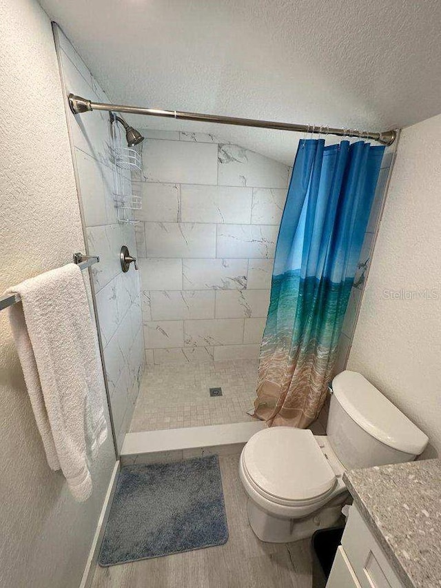 bathroom with a textured ceiling, vanity, toilet, and walk in shower