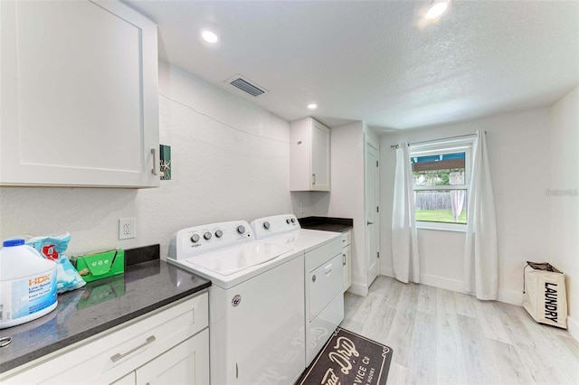 laundry room featuring light wood-type flooring, a textured ceiling, cabinets, and washer and dryer