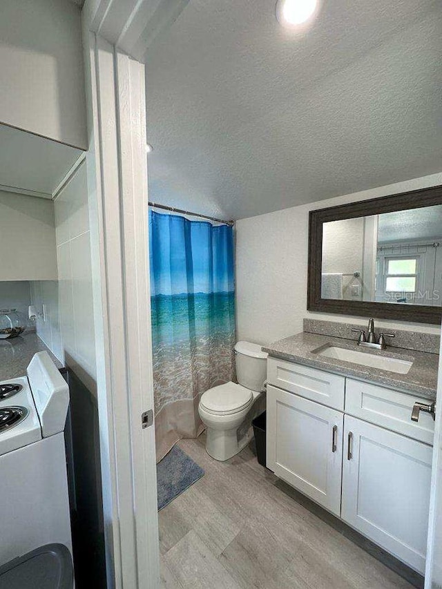 full bathroom featuring toilet, vanity, wood finished floors, a textured ceiling, and washer / dryer