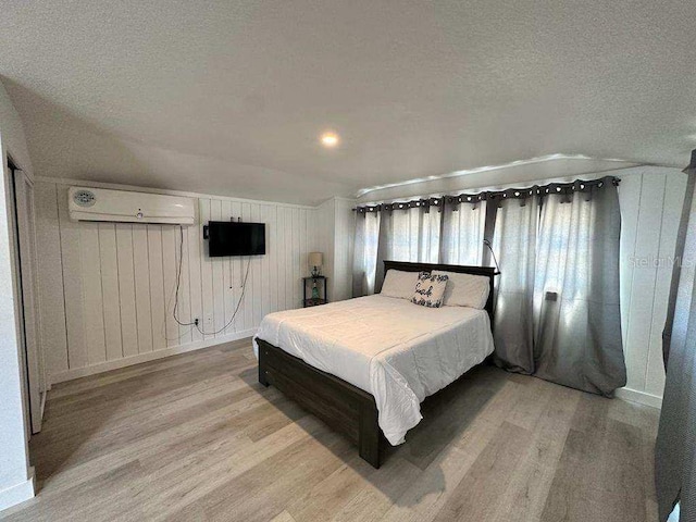 bedroom featuring a textured ceiling, wood walls, a wall mounted air conditioner, and light hardwood / wood-style floors