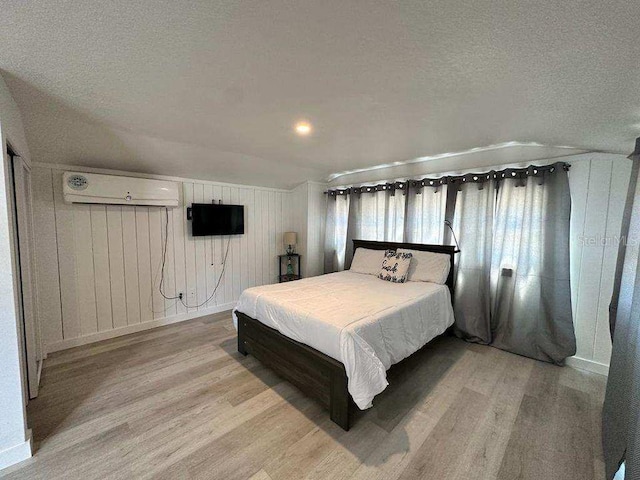 bedroom featuring a wall unit AC, light wood finished floors, and a textured ceiling