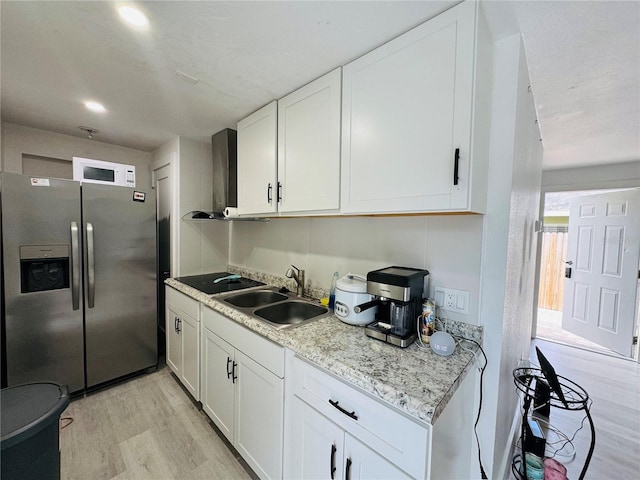 kitchen with white cabinetry, a sink, stainless steel refrigerator with ice dispenser, light wood-type flooring, and wall chimney range hood
