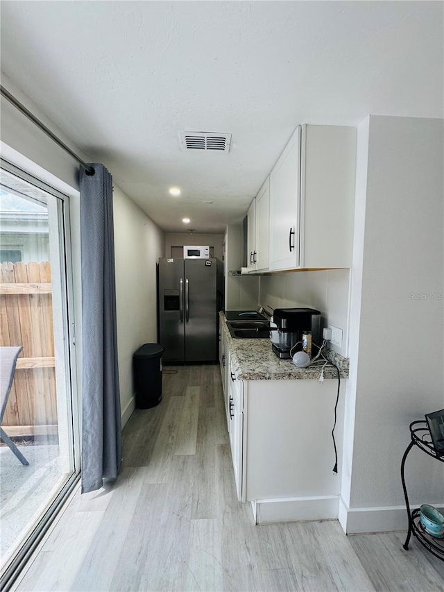 kitchen featuring stainless steel fridge, light hardwood / wood-style flooring, light stone counters, sink, and white cabinets