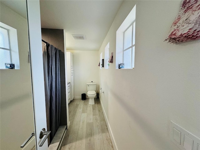 full bath with toilet, curtained shower, wood finished floors, baseboards, and visible vents