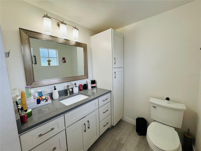 bathroom with toilet, vanity, baseboards, and wood finished floors
