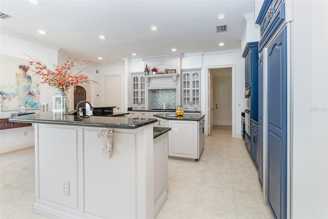 kitchen featuring light tile patterned floors, tasteful backsplash, a large island, white cabinetry, and dark stone counters