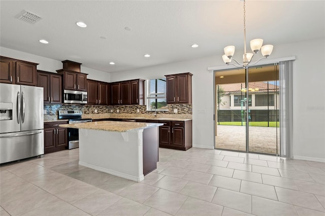 kitchen featuring a kitchen island, light stone counters, dark brown cabinetry, hanging light fixtures, and appliances with stainless steel finishes