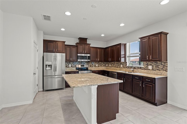 kitchen with a kitchen island, light stone countertops, tasteful backsplash, sink, and appliances with stainless steel finishes