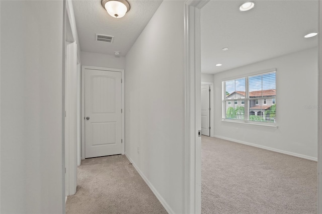 hallway with light carpet and a textured ceiling