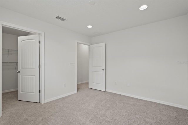 unfurnished bedroom featuring a spacious closet, a closet, and light colored carpet