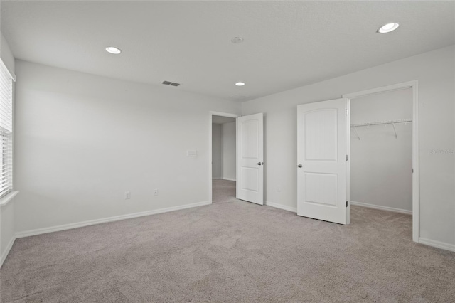 unfurnished bedroom with a spacious closet, a closet, and light colored carpet