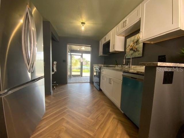 kitchen with light parquet flooring, appliances with stainless steel finishes, white cabinetry, and sink