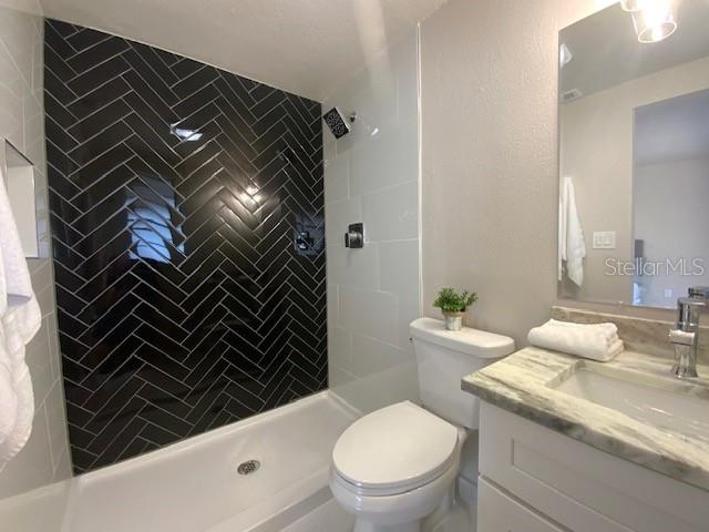 bathroom featuring tiled shower, toilet, and vanity