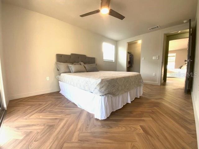 bedroom with parquet floors, a walk in closet, ceiling fan, and a closet