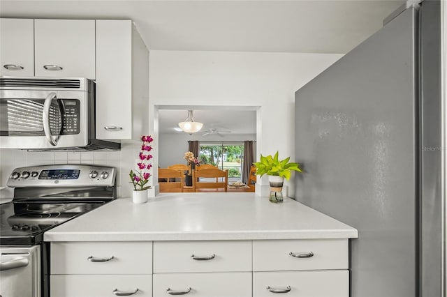 kitchen with decorative backsplash, white cabinets, stainless steel appliances, and hanging light fixtures