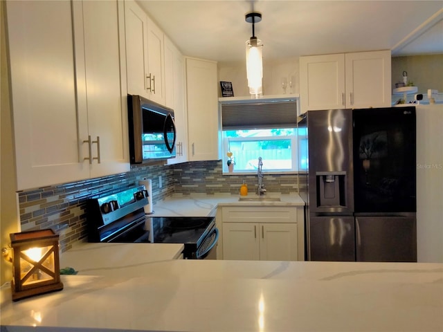 kitchen featuring pendant lighting, tasteful backsplash, sink, white cabinetry, and black appliances