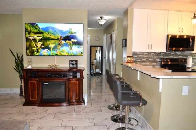 kitchen featuring decorative backsplash, white cabinets, a breakfast bar area, stainless steel appliances, and a textured ceiling