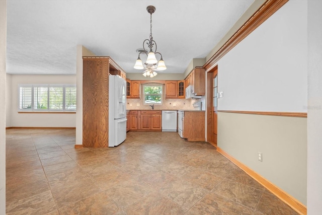 kitchen with plenty of natural light, backsplash, a notable chandelier, and white appliances