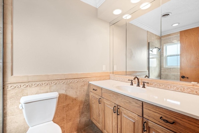 bathroom with vanity, a tile shower, crown molding, toilet, and tile walls