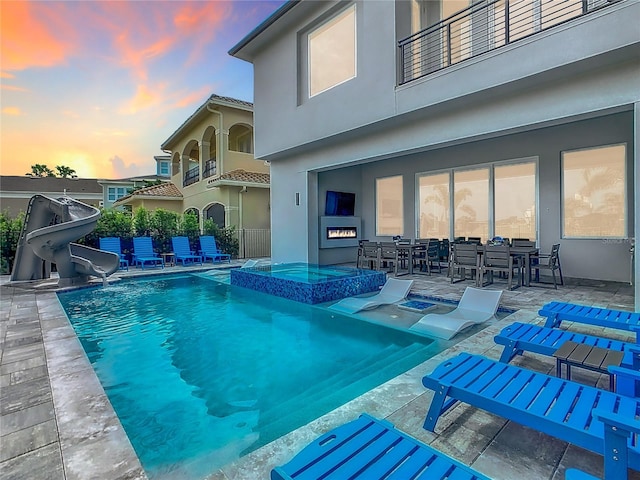 pool at dusk with a water slide and a patio area