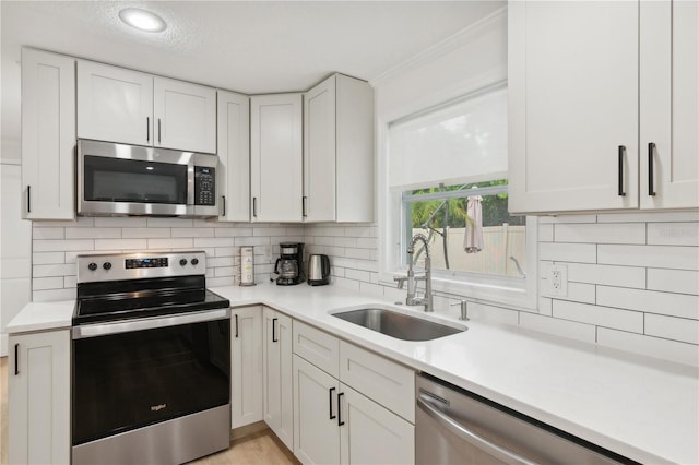 kitchen with sink, white cabinetry, backsplash, stainless steel appliances, and ornamental molding