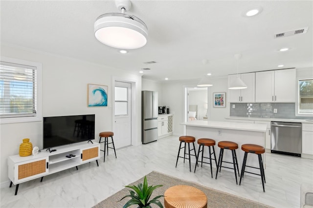 kitchen featuring white cabinets, appliances with stainless steel finishes, light countertops, a kitchen bar, and backsplash