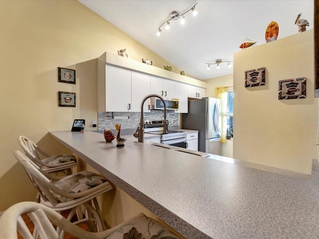 kitchen with rail lighting, white cabinetry, vaulted ceiling, appliances with stainless steel finishes, and decorative backsplash