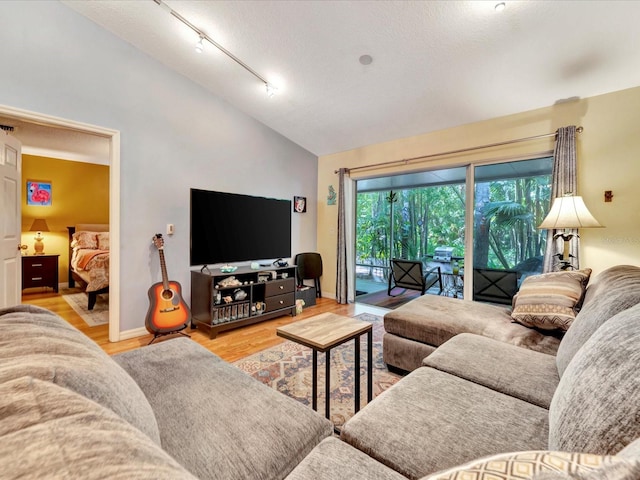 living room featuring lofted ceiling, light hardwood / wood-style floors, rail lighting, and a textured ceiling