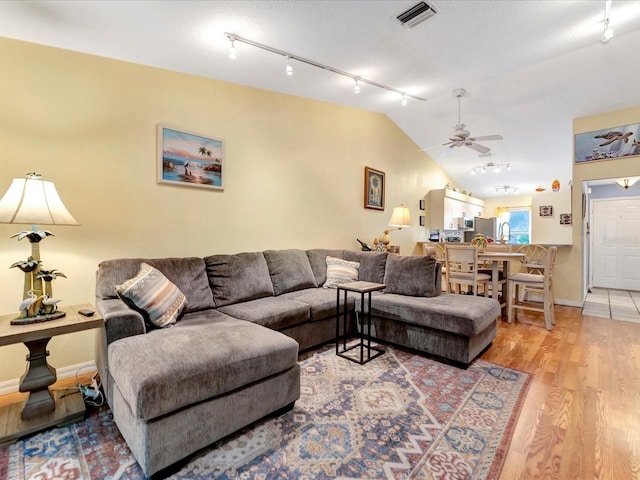 living room with hardwood / wood-style flooring, ceiling fan, rail lighting, and vaulted ceiling