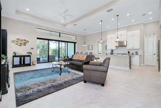 living room with a raised ceiling, ceiling fan, and ornamental molding