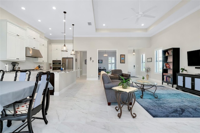 living room with a raised ceiling, ceiling fan, and a high ceiling