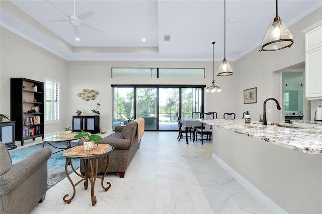 living room featuring ceiling fan, a raised ceiling, ornamental molding, and sink