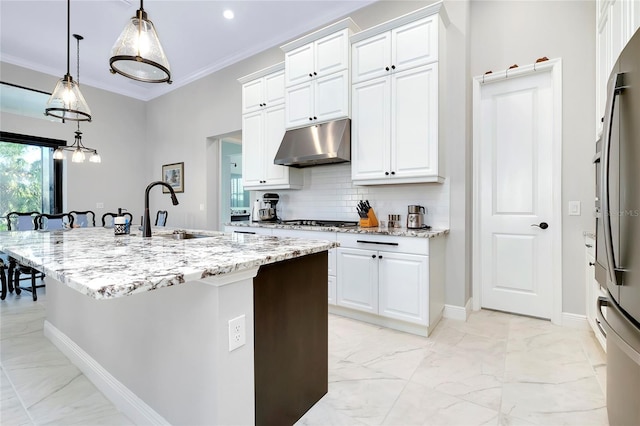 kitchen featuring a sink, marble finish floor, crown molding, under cabinet range hood, and backsplash