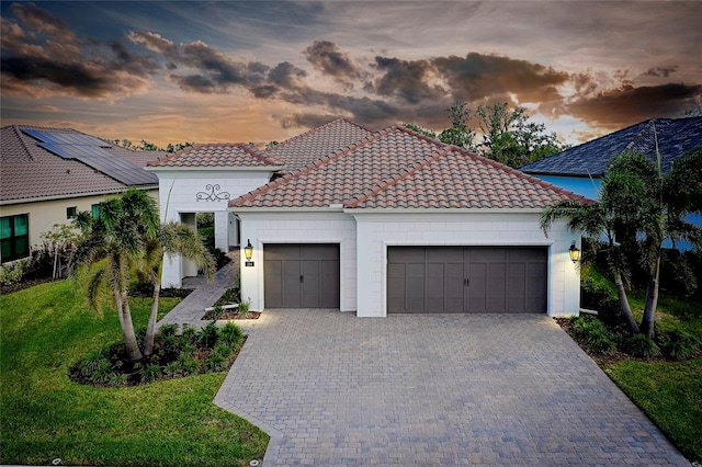 mediterranean / spanish home with a yard, decorative driveway, an attached garage, and a tile roof