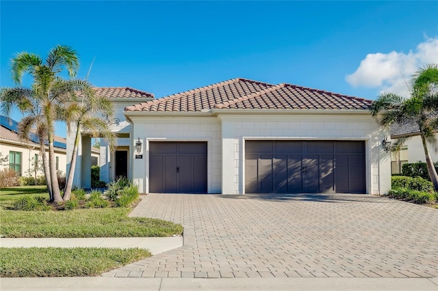 mediterranean / spanish house featuring a garage, decorative driveway, and a tiled roof