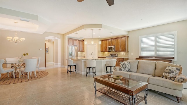 tiled living room featuring ceiling fan with notable chandelier and sink