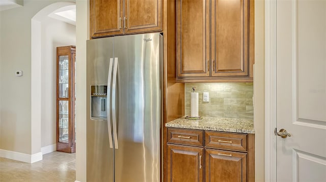 kitchen featuring stainless steel fridge, light tile patterned flooring, light stone counters, and tasteful backsplash