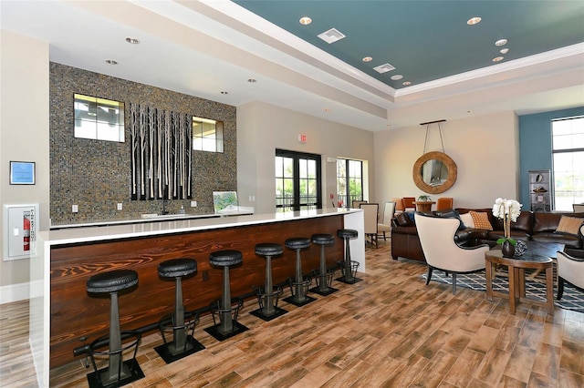 bar with ornamental molding, decorative backsplash, a tray ceiling, and hardwood / wood-style floors