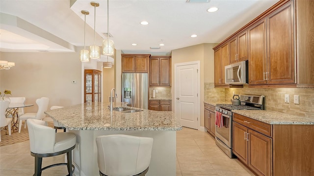 kitchen featuring a kitchen breakfast bar, hanging light fixtures, stainless steel appliances, a center island with sink, and sink