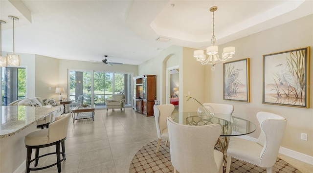 tiled dining space featuring ceiling fan with notable chandelier and a raised ceiling