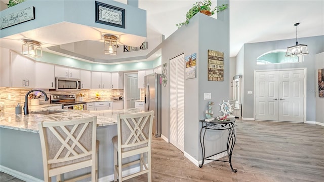 kitchen with white cabinets, appliances with stainless steel finishes, light wood-type flooring, a high ceiling, and sink