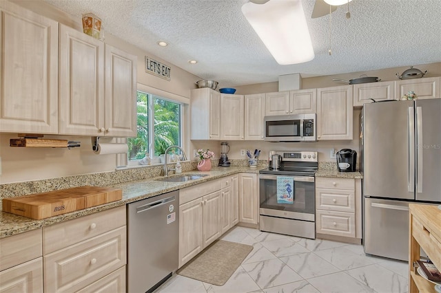 kitchen featuring a textured ceiling, stainless steel appliances, sink, and light stone counters