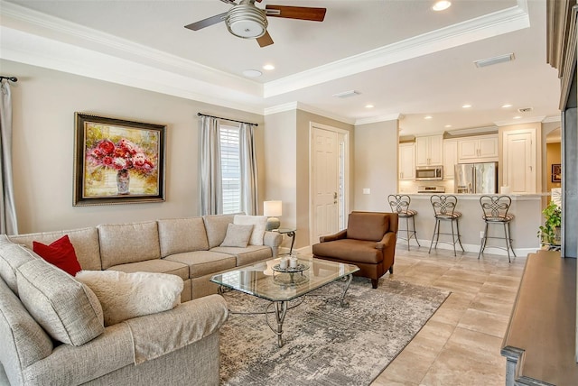 tiled living room featuring a raised ceiling, ornamental molding, and ceiling fan