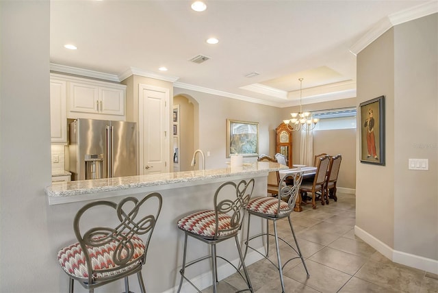 kitchen featuring a kitchen breakfast bar, light stone countertops, pendant lighting, an inviting chandelier, and high end fridge