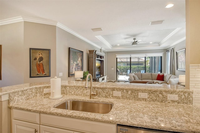 kitchen with ceiling fan, light stone counters, a raised ceiling, ornamental molding, and sink