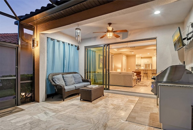 patio terrace at dusk with an outdoor kitchen, glass enclosure, ceiling fan, and an outdoor living space